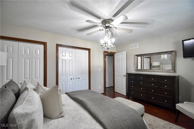 Bedroom featuring multiple closets, dark wood-type flooring, a textured ceiling, and a ceiling fan | Image 15