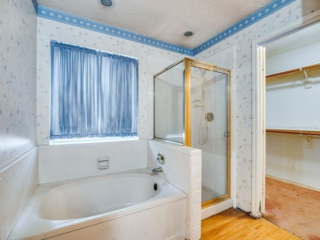 Bathroom with wallpapered walls, a garden tub, a stall shower, a spacious closet, and wood finished floors | Image 11