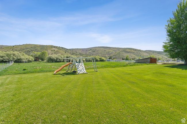 View of grassy yard featuring a playground, a mountain view, and an outdoor structure | Image 62