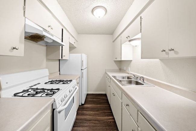 Kitchen with a textured ceiling, white appliances, dark wood-type flooring, under cabinet range hood, and a sink | Image 5
