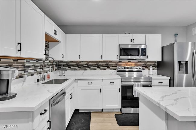 Kitchen with a sink, stainless steel appliances, light wood-type flooring, light stone counters, and white cabinetry | Image 13