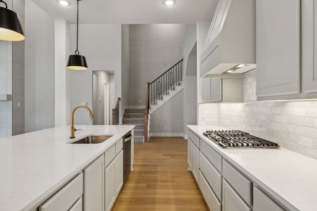 Kitchen with appliances with stainless steel finishes, custom range hood, light wood-style flooring, hanging light fixtures, and white cabinets | Image 10