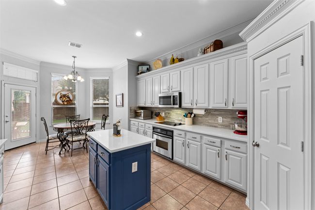 Kitchen featuring stainless steel appliances, blue cabinets, white cabinetry, decorative backsplash, and crown molding | Image 8