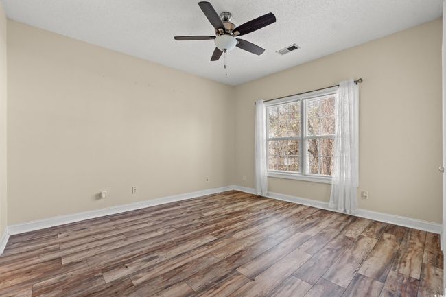 Empty room with wood finished floors, baseboards, ceiling fan, and visible vents | Image 11