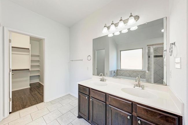 Primary bathroom featuring tile patterned floors, a walk in closet, a shower stall, double vanity, and baseboards | Image 23