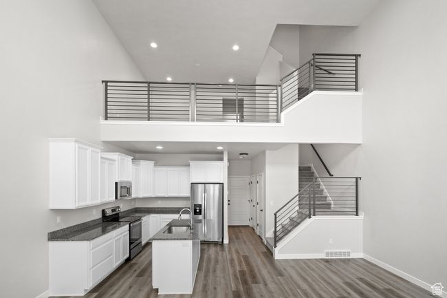 Kitchen with appliances with stainless steel finishes, a high ceiling, white cabinets, dark stone countertops, and an island with sink | Image 12