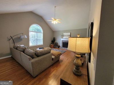 Great room featuring vaulted ceiling, stacked stone fireplace, hardwood flooring, ceilingfan and arched doorway to kitchen | Image 2