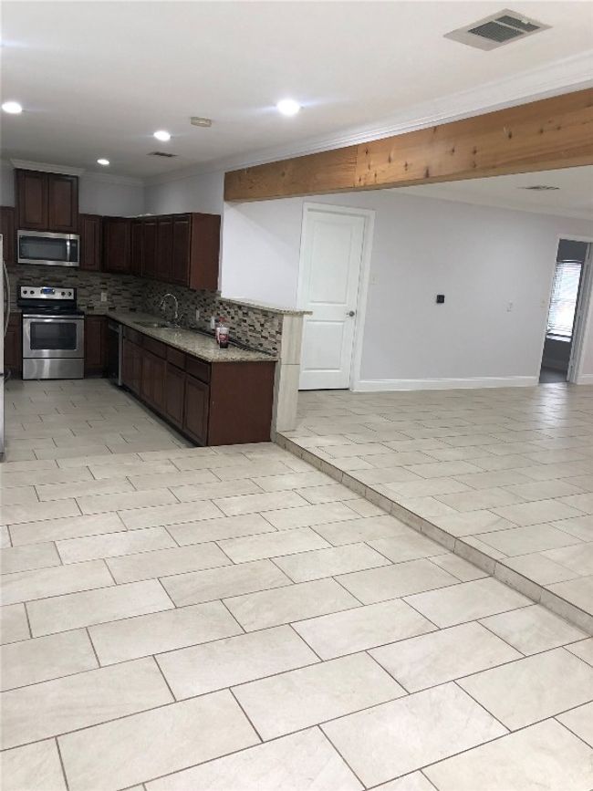 Kitchen with stainless steel appliances, tasteful backsplash, open floor plan, dark brown cabinetry, and light stone counters | Image 18