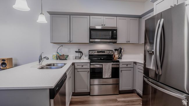 Kitchen with a peninsula, a sink, gray cabinets, light countertops, and appliances with stainless steel finishes | Image 12