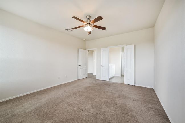 Spacious primary bedroom with neutral carpeting, featuring a ceiling fan and ample natural light. It has a walk-in closet and an en-suite bathroom with dual doors, enhancing convenience and privacy. | Image 9