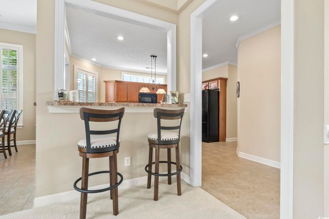 Kitchen with brown cabinets, a breakfast bar, a healthy amount of sunlight, black appliances, and ornamental molding | Image 6