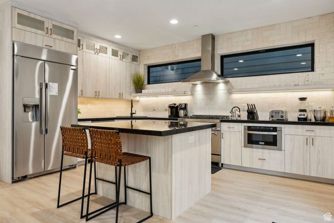 Kitchen featuring wall chimney range hood, a center island, sink, appliances with stainless steel finishes, and a breakfast bar area | Image 15