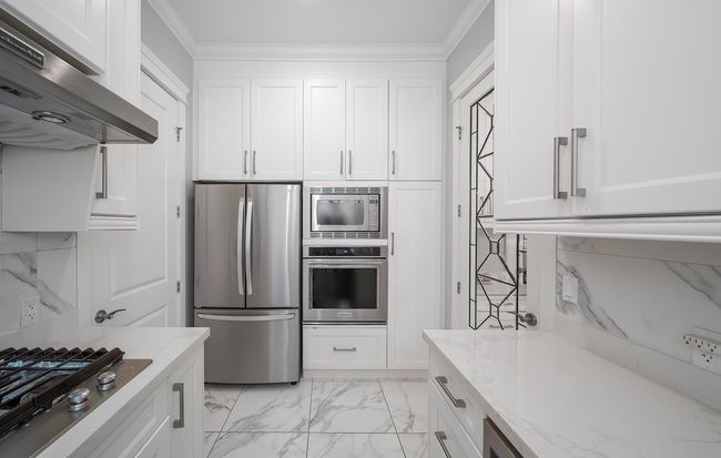 Kitchen featuring under cabinet range hood, appliances with stainless steel finishes, light stone counters, and white cabinetry | Image 11