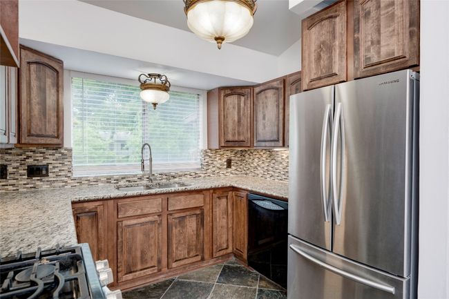 Kitchen with a sink, black dishwasher, freestanding refrigerator, decorative backsplash, and stone finish flooring | Image 13