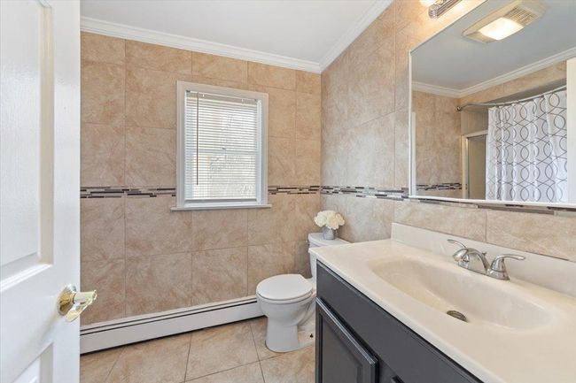 Bathroom featuring tile walls, crown molding, toilet, baseboard heating, and tile patterned flooring | Image 9