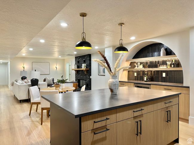 Kitchen with a textured ceiling, a center island, light wood-style flooring, recessed lighting, and dark countertops | Image 28