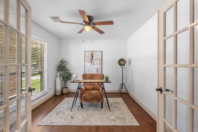 Home showcases a bright home office with French doors, hardwood floors, and a large window providing natural light. It features a ceiling fan, modern decor, and a cozy setup with a desk and chair. Perfect for a productive work-from-home environment. | Image 6