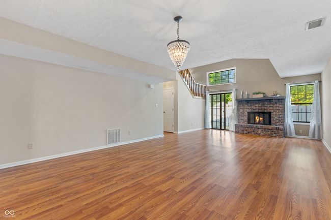 unfurnished living room featuring wood finished floors, a textured ceiling, a chandelier, baseboards, and a fireplace | Image 13