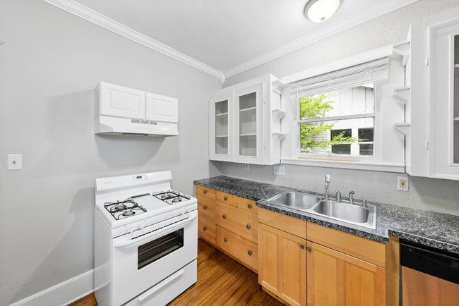 Kitchen featuring white gas stove, a sink, stainless steel dishwasher, under cabinet range hood, and ornamental molding | Image 9