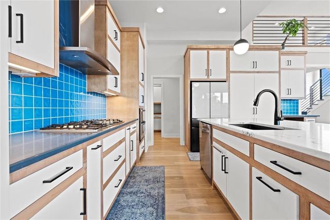 Kitchen with wall chimney range hood, stainless steel appliances, hanging light fixtures, light wood-type flooring, and white cabinetry | Image 15