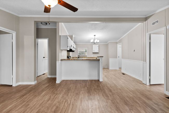 Kitchen featuring light wood finished floors, a chandelier, a peninsula, a textured ceiling, and crown molding | Image 14