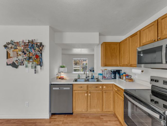 Kitchen with stainless steel appliances, a sink, light countertops, and light wood-type flooring | Image 12