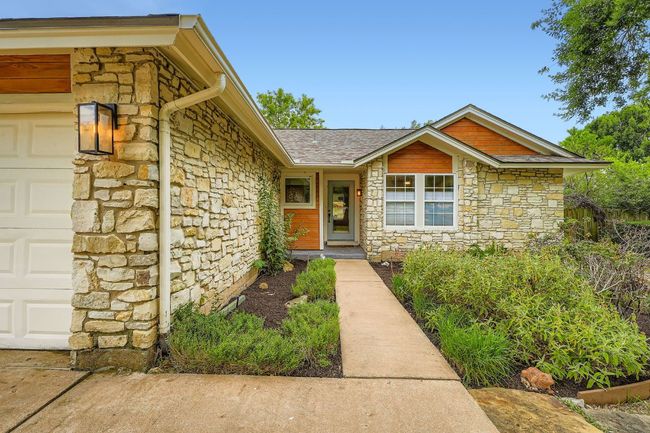 Doorway to property with stone siding, an attached garage, and a shingled roof | Image 5