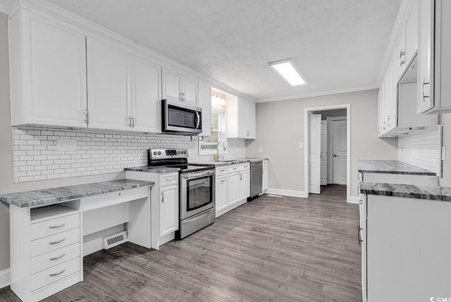 Kitchen with stainless steel appliances, wood finished floors, a textured ceiling, tasteful backsplash, and white cabinetry | Image 12