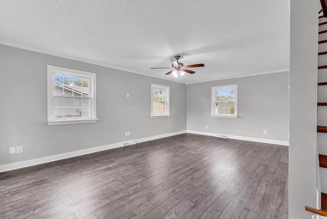 Empty room featuring crown molding, a textured ceiling, ceiling fan, dark wood-style floors, and stairs | Image 4