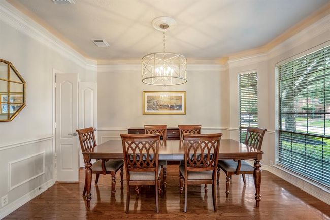 An elegant dining room features updated custom lighting, chair railings, crown molding and rich hardwood floors with an expansive wall of windows. | Image 9