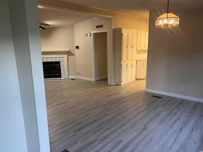 Unfurnished living room with a chandelier, wood finished floors, a textured ceiling, a tiled fireplace, and baseboards | Image 10