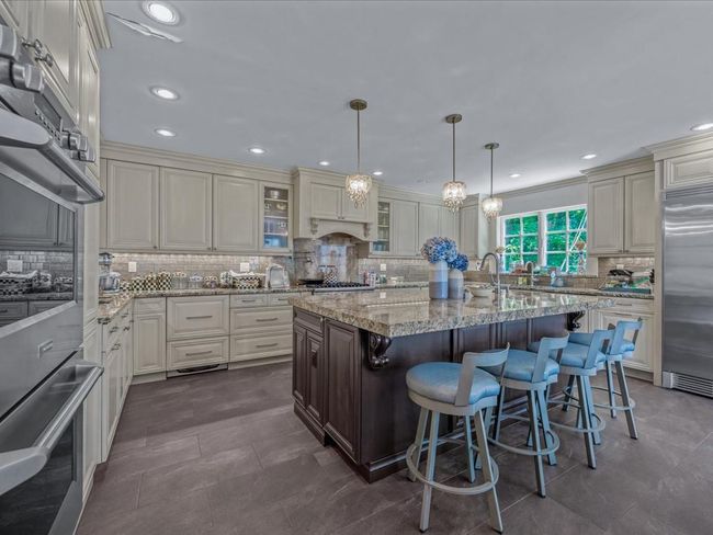 Kitchen with stainless steel appliances, backsplash, glass insert cabinets, a center island with sink, and light stone countertops | Image 7