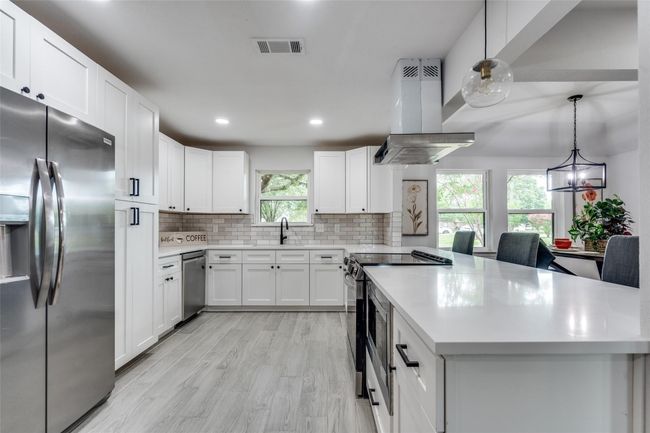 Kitchen featuring stainless steel appliances, decorative backsplash, hanging light fixtures, recessed lighting, and island range hood | Image 8