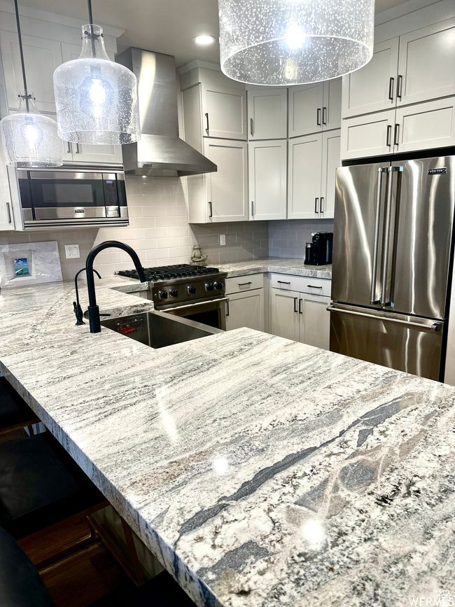 Kitchen featuring sink, backsplash, high end appliances, light stone counters, and wall chimney range hood | Image 5