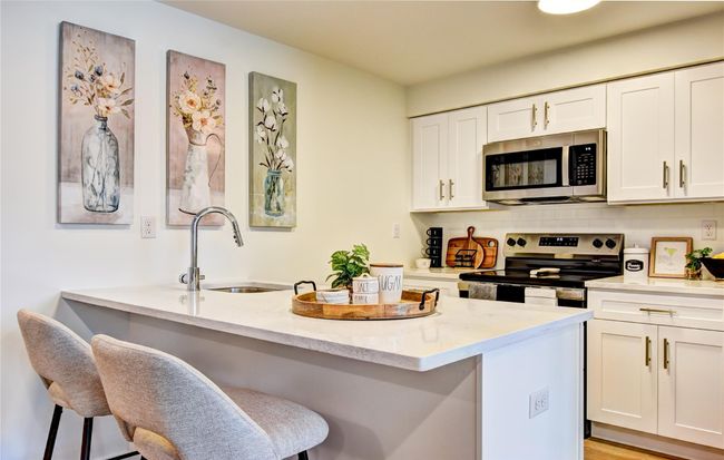 Kitchen featuring white cabinetry, a sink, decorative backsplash, appliances with stainless steel finishes, and a kitchen bar | Image 10