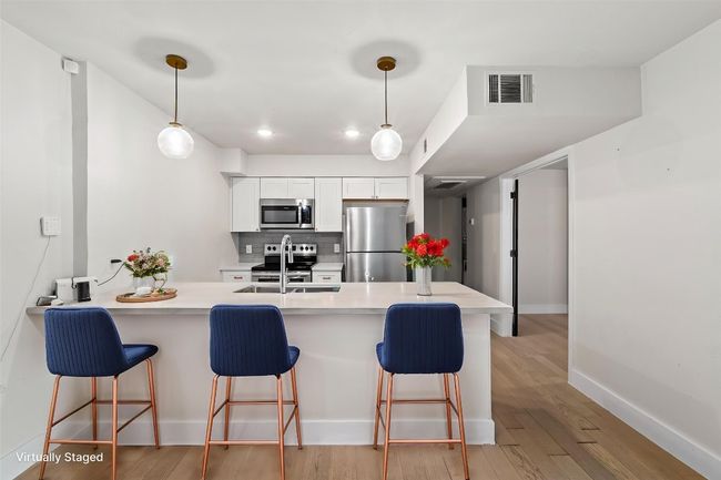 Kitchen with stainless steel appliances, a sink, a kitchen bar, a peninsula, and white cabinetry | Image 4
