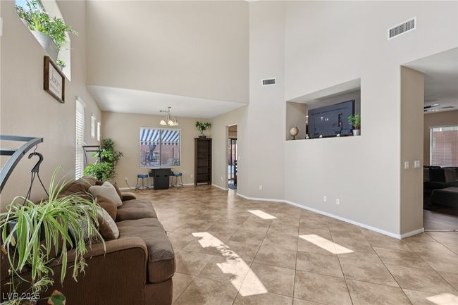 Living room featuring a towering ceiling, light tile patterned flooring, a chandelier, and baseboards | Image 8