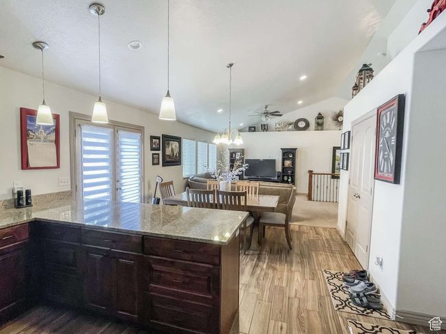 Kitchen featuring a peninsula, wood finished floors, light stone countertops, lofted ceiling, and a ceiling fan | Image 16