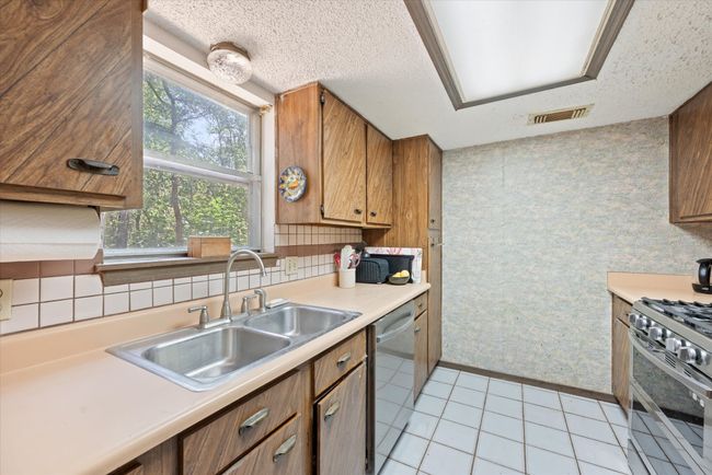 Kitchen featuring sink, light tile patterned floors, a textured ceiling, and appliances with stainless steel finishes | Image 19