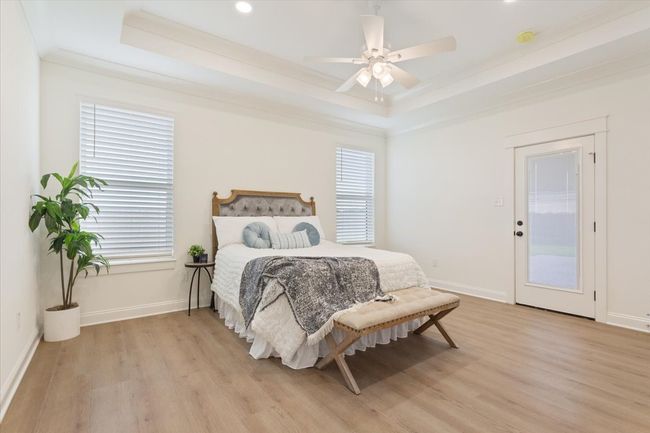 Bedroom with a tray ceiling, light wood-type flooring, multiple windows, crown molding, and a ceiling fan | Image 15