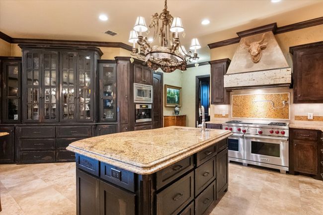 Kitchen featuring stainless steel appliances, premium range hood, a sink, a chandelier, and a kitchen island | Image 11