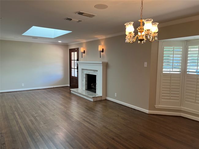Unfurnished living room featuring ornamental molding, dark wood-style floors, a skylight, a premium fireplace, and a chandelier | Image 9