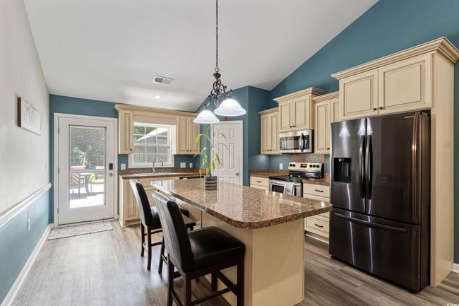 Kitchen featuring appliances with stainless steel finishes, cream cabinets, wood finished floors, a kitchen island, and lofted ceiling | Image 12