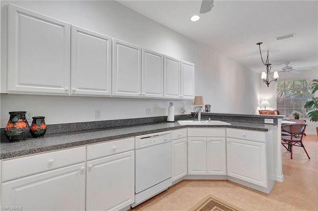 Kitchen with white cabinetry, kitchen peninsula, white dishwasher, ceiling fan, and sink | Image 12