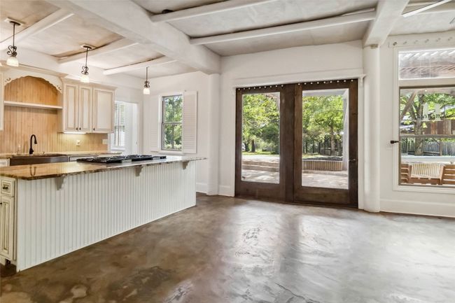 Front entry to kitchen featuring cream cabinetry, finished concrete floors, stainless steel gas stovetop, a kitchen breakfast bar, and beam ceiling | Image 7