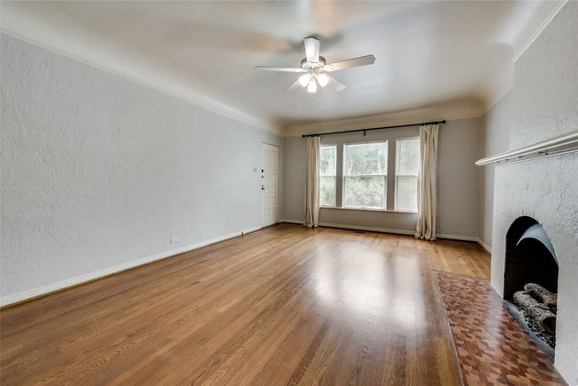 Unfurnished living room with ceiling fan, wood finished floors, a fireplace, and a textured wall | Image 8