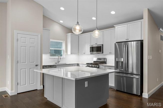 Kitchen featuring stainless steel appliances, decorative backsplash, dark wood-type flooring, a center island, and lofted ceiling | Image 7
