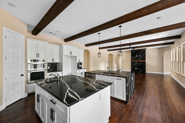 Kitchen featuring arched walkways, stainless steel appliances, dark countertops, a sink, and an island with sink | Image 26
