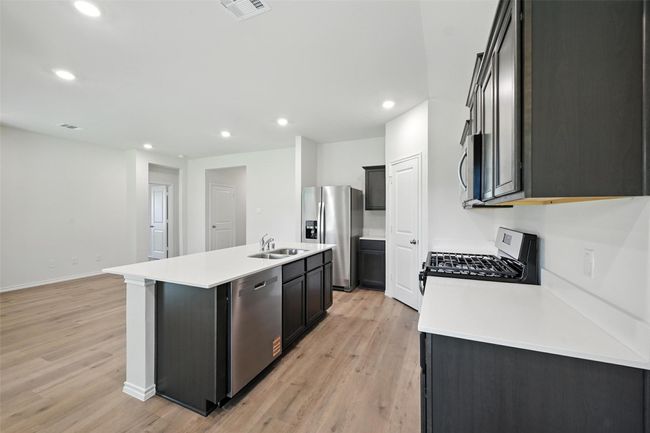 Kitchen featuring stainless steel appliances, light wood finished floors, recessed lighting, a center island with sink, and light countertops | Image 4