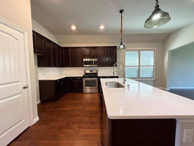 Kitchen featuring stainless steel appliances, a sink, dark brown cabinets, dark wood-type flooring, and decorative light fixtures | Image 5